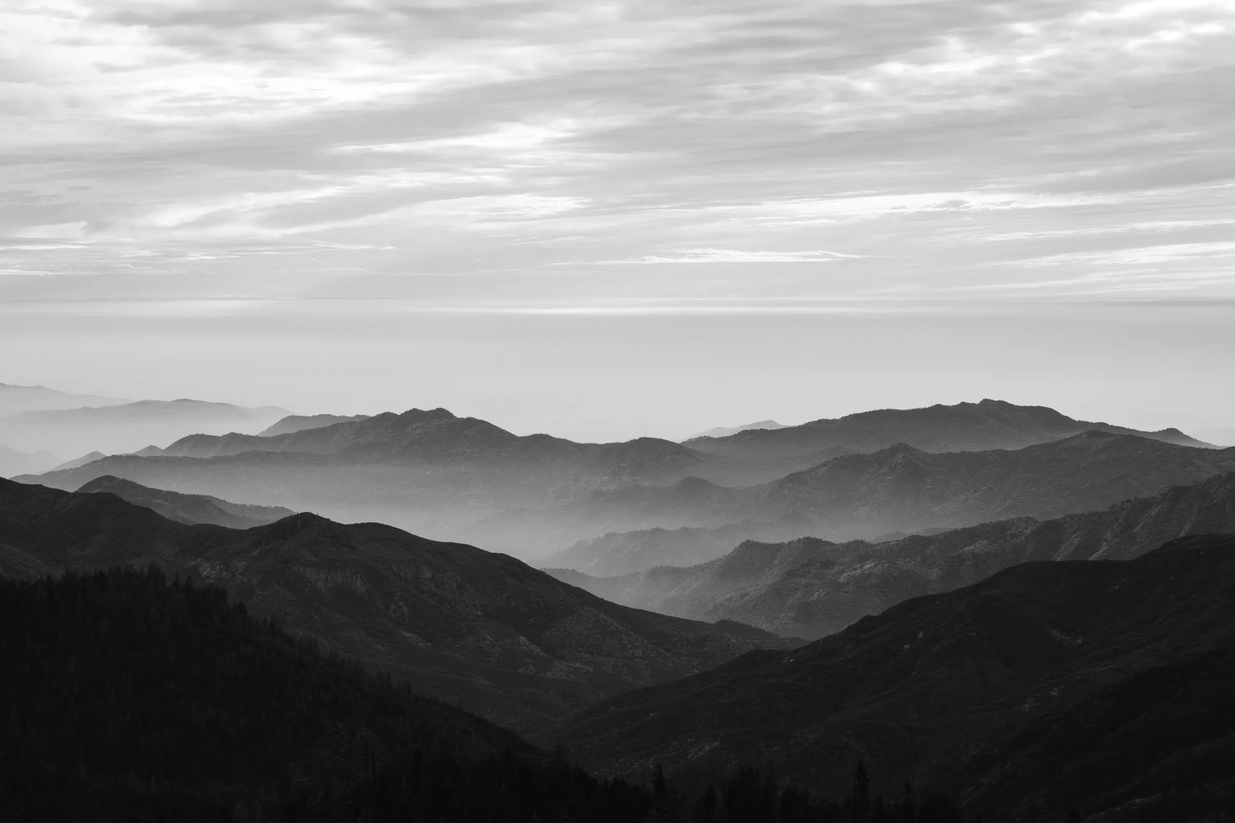 Black and white mountain ridges receding into haze in layered bands under a pale overcast sky