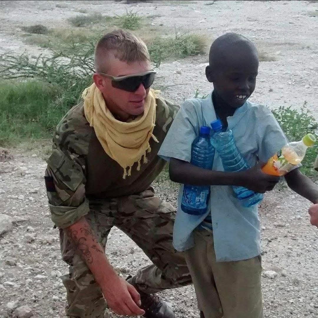 Conor during his Army service, kneeling beside a smiling child.